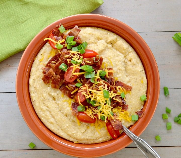 Overhead view of bowl with cheese grits topped with bacon, tomatoes and green onions