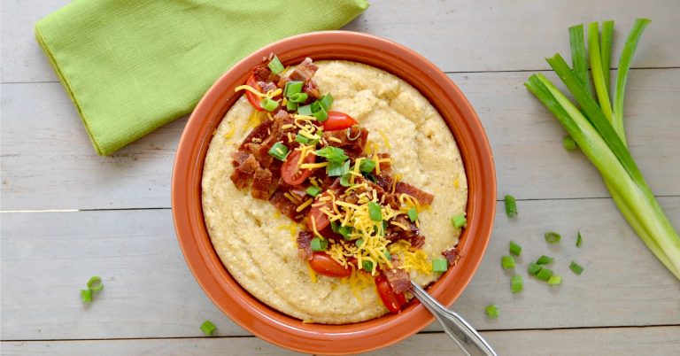 Overhead view of bowl with cheese grits topped with bacon, tomatoes and green onions
