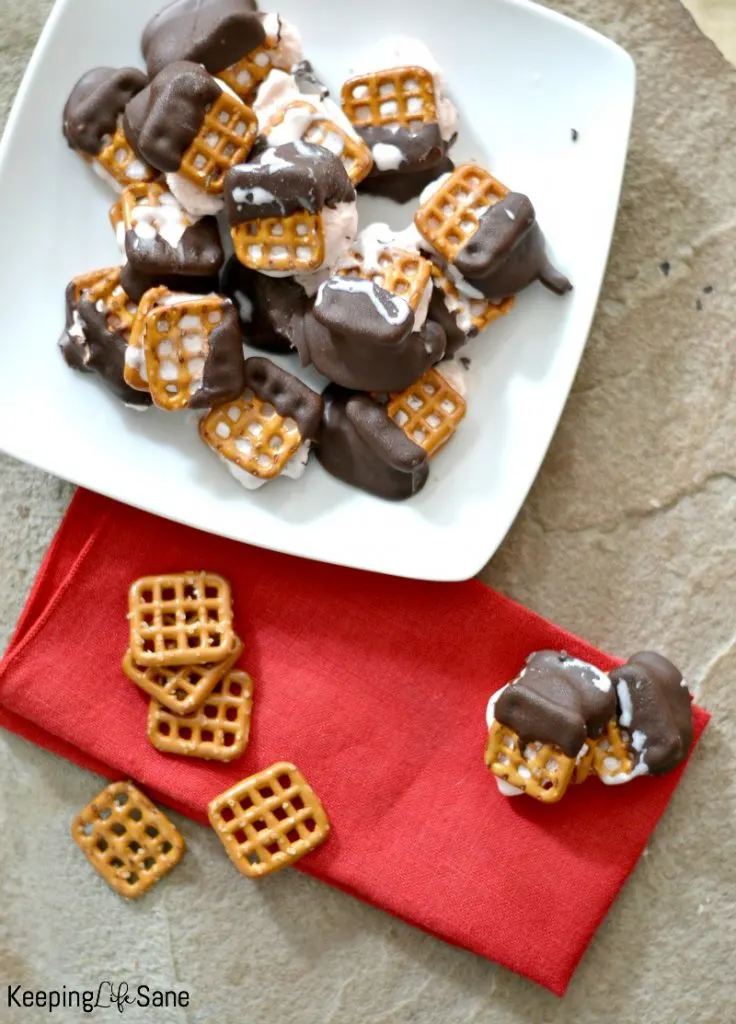 overhead view of ice cream bites with pretzels and dipped in chocolate on white plate with red napkin