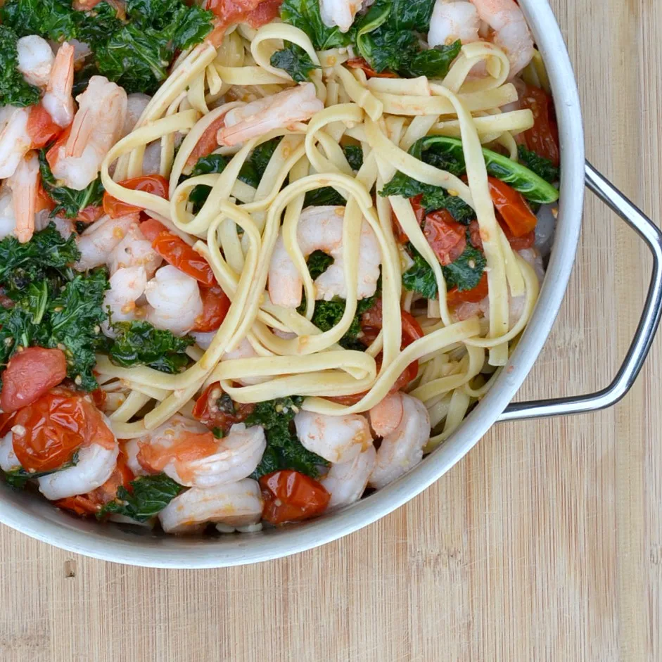 overhead view large pot filled with cooked kale, shrimp, pasta, red cherry tomatoes