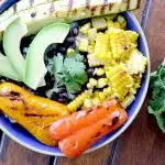 overhead view of burrito bowl with grilled corn, avocados, peppers, with cilantro, black beans and sliced avocado