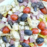overhead closeup view of antipasto with rotini, grape tomatoes, olives, cheese cubes, artichokes, salami and cheese cubes
