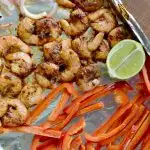 overhead and closeup view of cooked shrimp, red peppers and lime on foil line baking sheet
