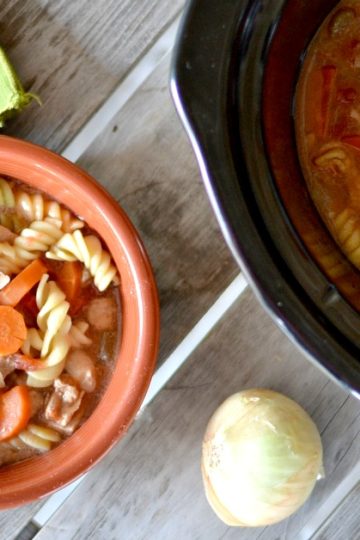 bowl of chicken noodle soup with crockpot with soup in it