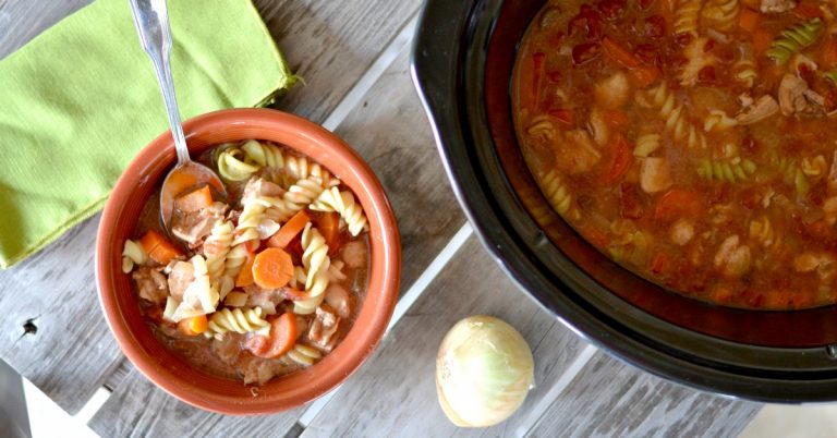 bowl of chicken noodle soup with crockpot with soup in it