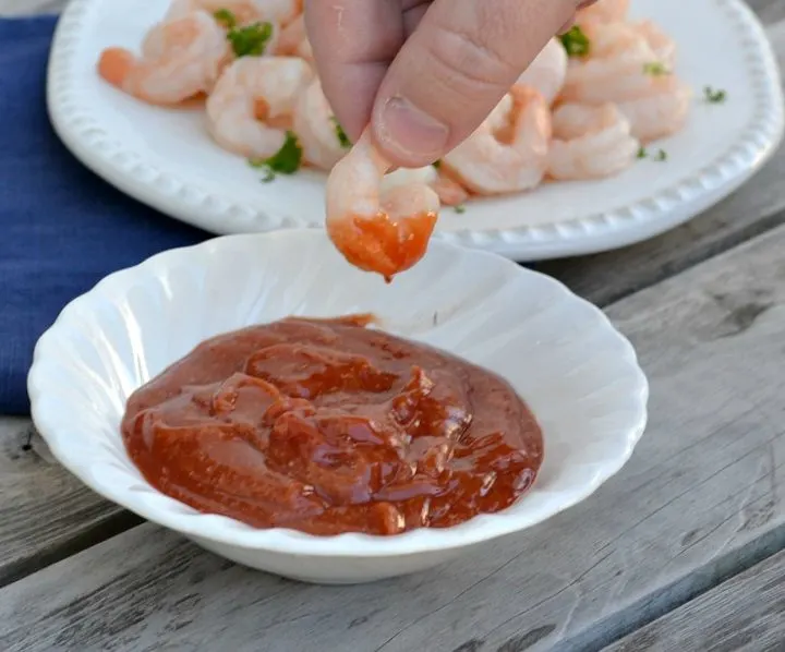 white bowl with cocktail sauce and a hand that dipped a shrimp in