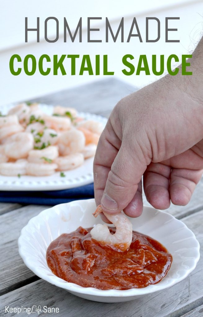 small white bowl with homemade cocktail sauce with hand dipping a shrimp in it