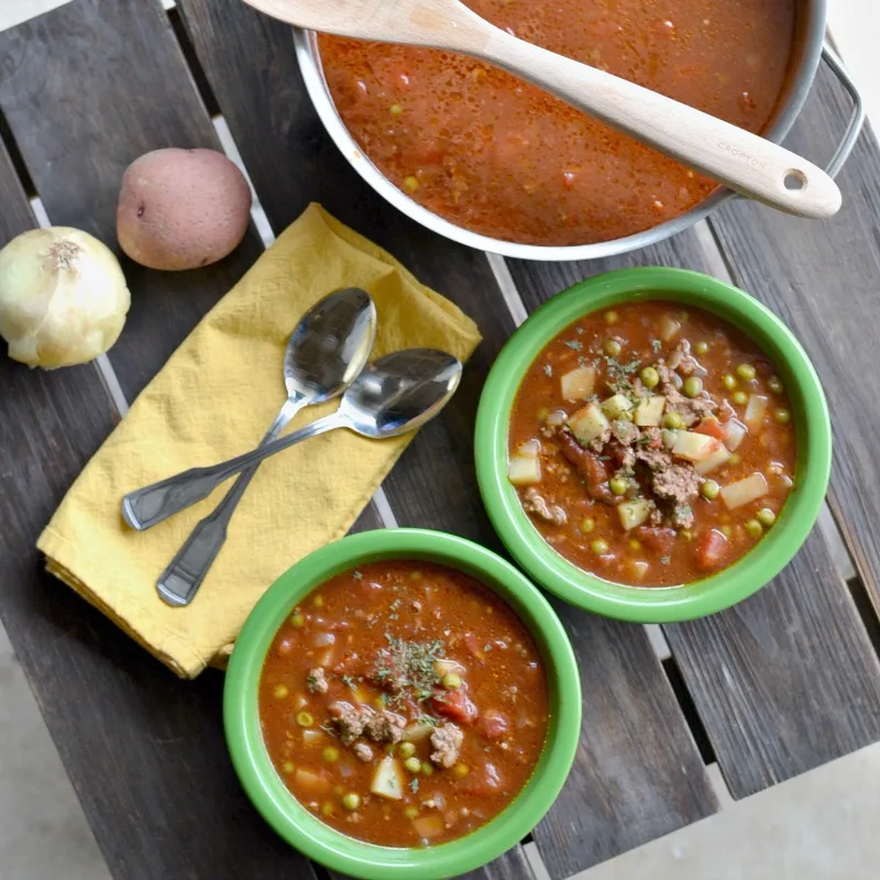 over head view of hamburger tomato soup in pot and in two green bowls on wooden table
