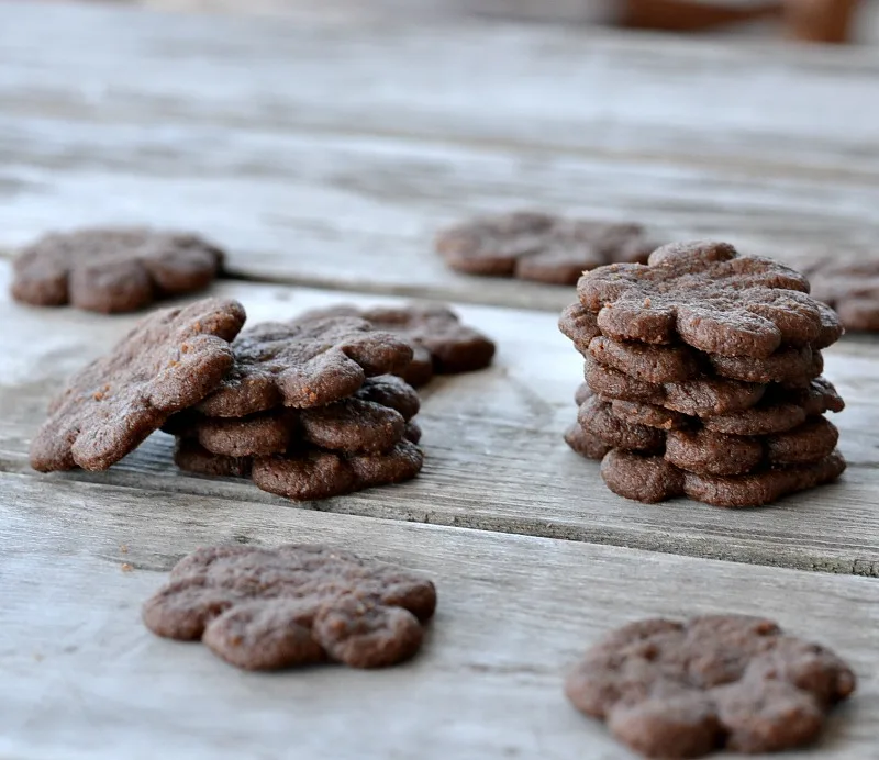 lots of eggless chocolate cookies shaped like flowers stacked on a wooden table