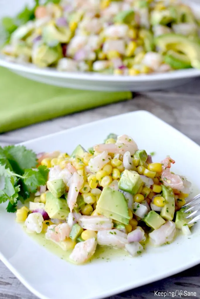 shrimp avocado salad with corn on white plate with cilantro garnish