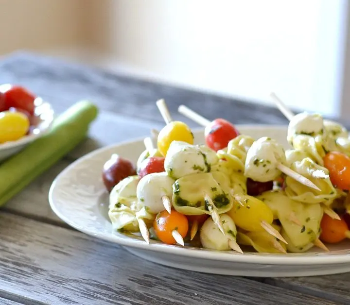 white platter with a bunch of tomatoes, mozzarella and tortellini skewers.