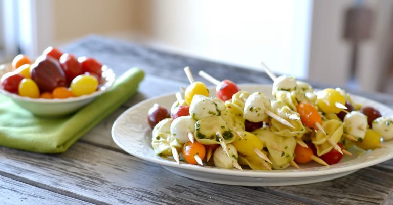 white platter with a bunch of tomatoes, mozzarella and tortellini skewers.