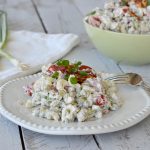Creamy pea salad on white plate topped with crumbled bacon and chives with green bowl with pea salad in background