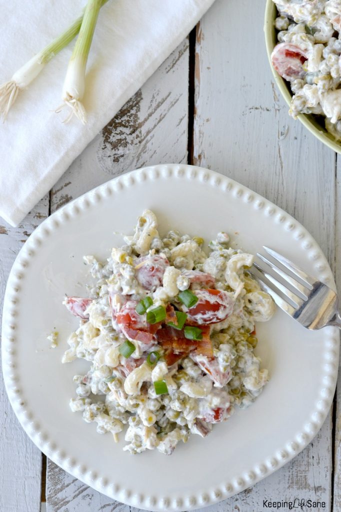 Overhead view of creamy peas salad on white plate topped with crumbled bacon and chives with green bowl with pea salad in background