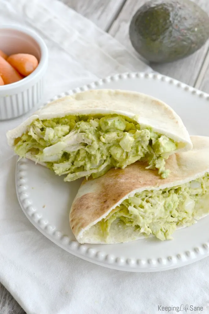 split pita bread with green chicken salad without mayo with avocados on white plate.