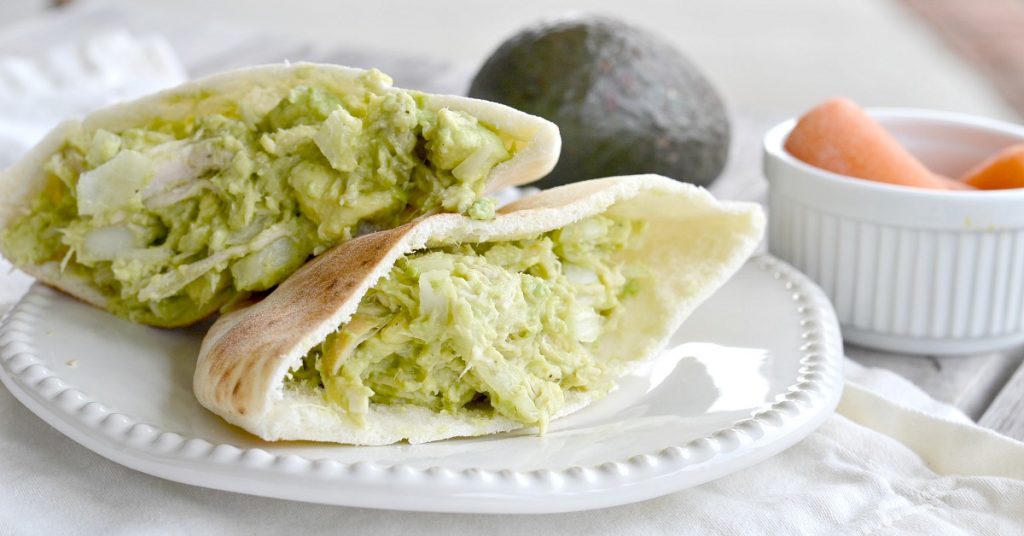 split pita bread with green chicken salad without mayo with avocados on white plate.
