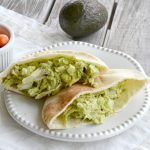 split pita bread with green avocado chicken salad inside on a white plate.