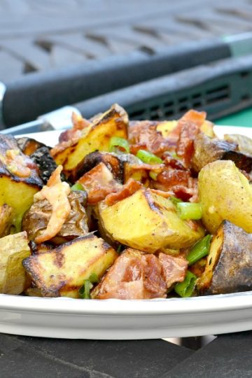 White plate with grilled potato salad sitting on black outside table with grilling tongs and green napkin