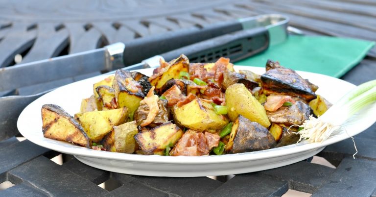 White plate with grilled potato salad sitting on black outside table with grilling tongs and green napkin