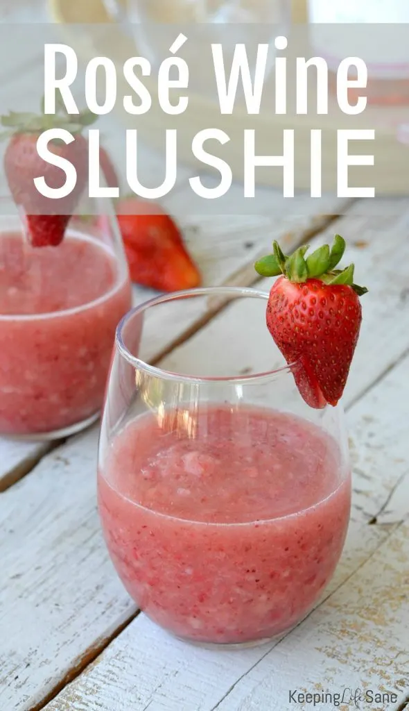 wine glass with frozen strawberry wine slushie on wooden boards with fresh strawberries laying about and one on the wine glass