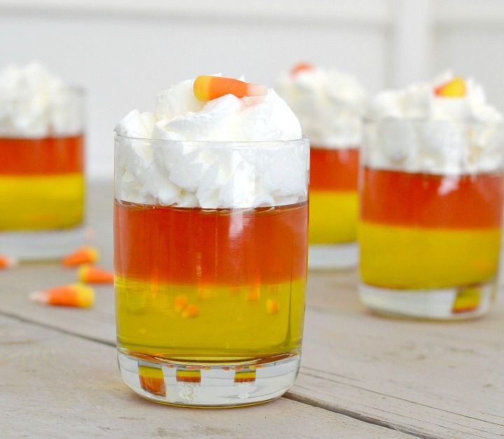 candy corn jello cups with yellow and orange jellos with whipped cream on top in clean glasses