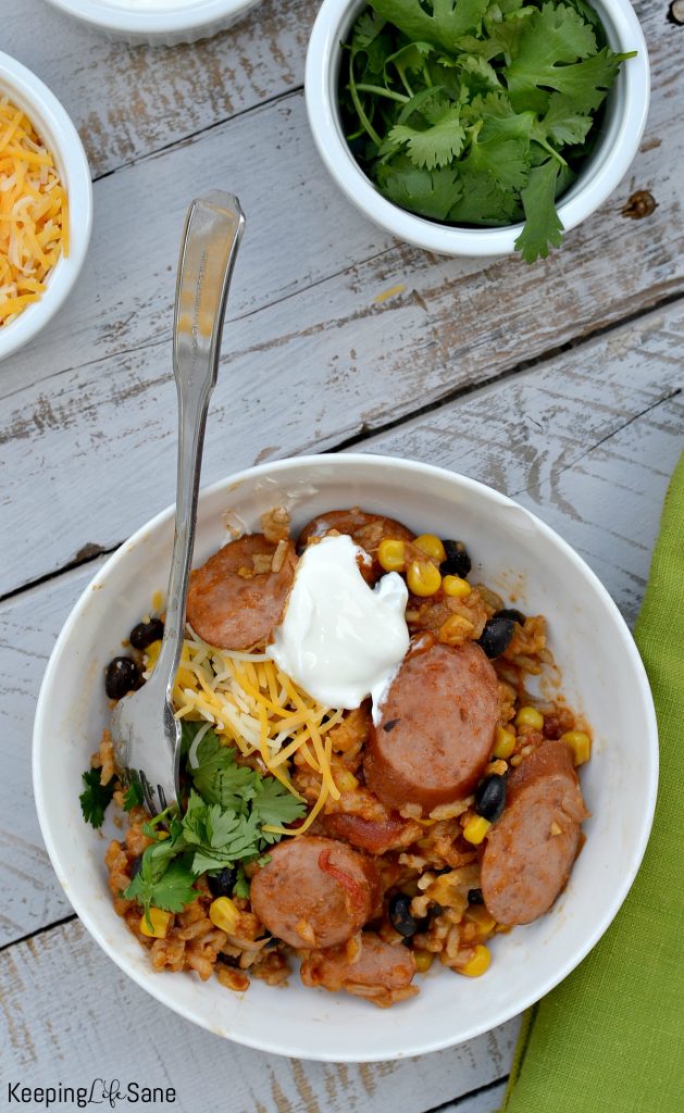 overhead view of mexican sausage casserole in white bowl with shredded cheese, sour cream and cilantro for garnish