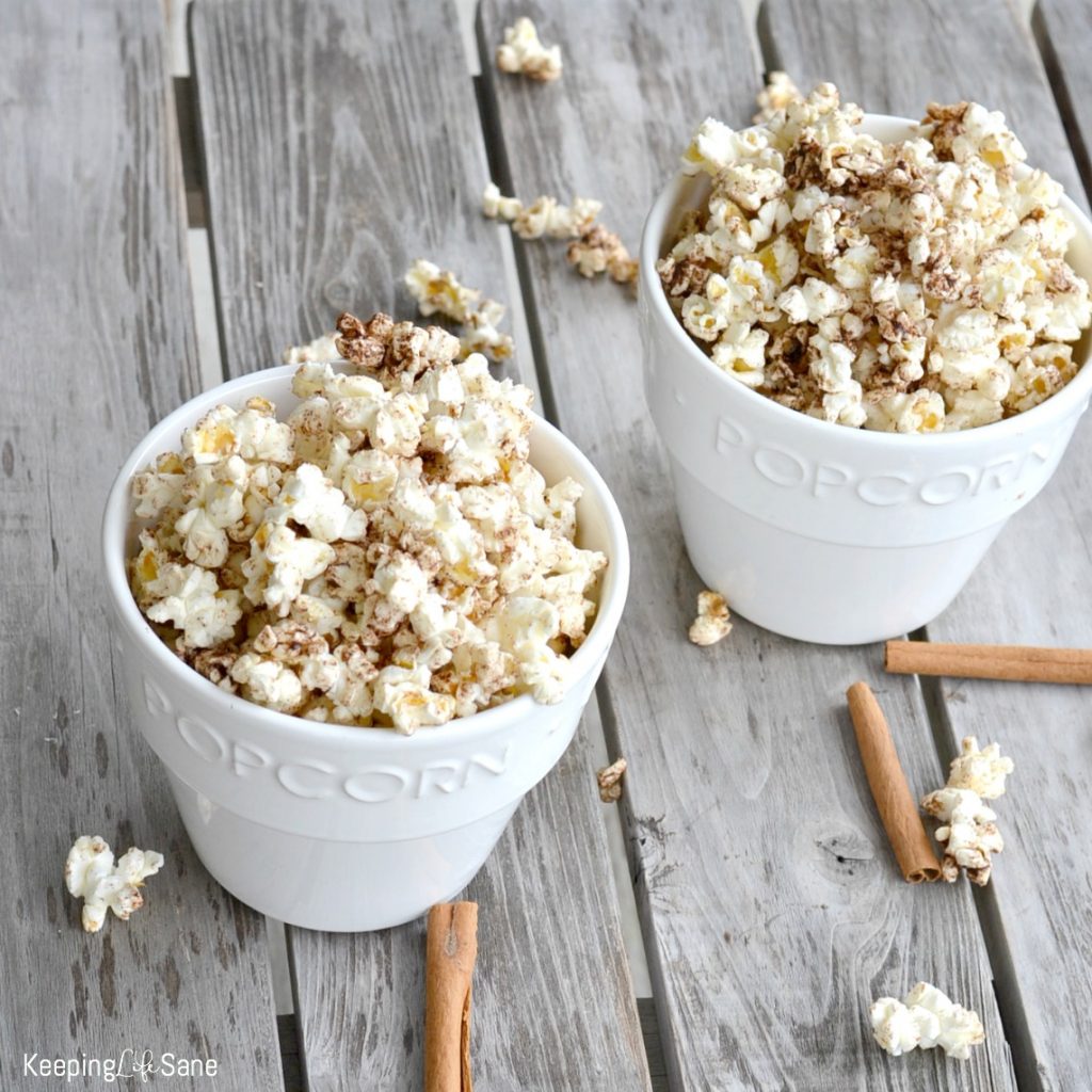 two white popcorn bowls with cinnamon honey popcorn overflowing on wooden table