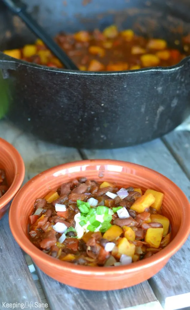 Cast iron pot with butternut squash chili with a bowl of chili topped with sour cream and green onions