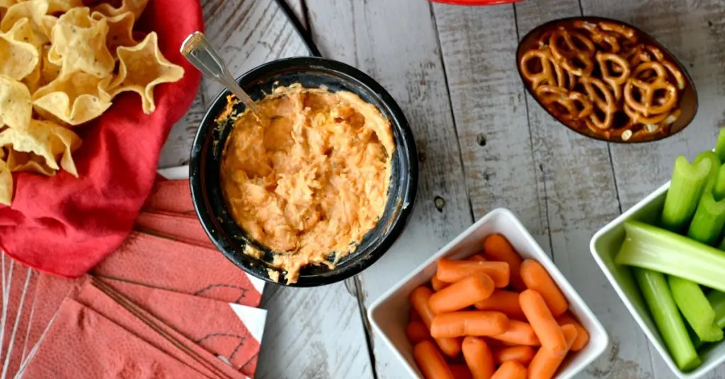 Overhead view of mini slow cooker with buffalo chicken dip with carrots, celery, pretzels and chips on the side