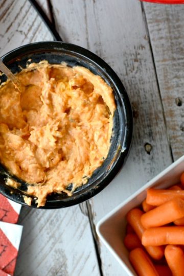 Overhead view of mini slow cooker with buffalo chicken dip with carrots, celery, pretzels and chips on the side