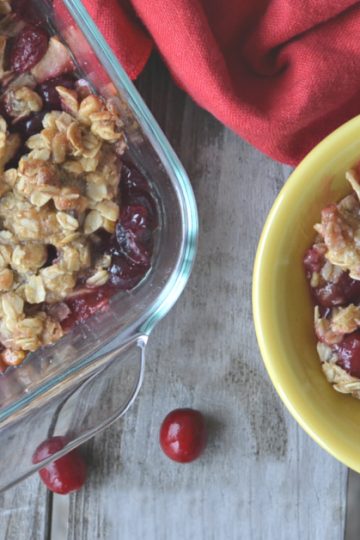 overhead view of apple cranberry crisp in yellow bowl on wooden table with baking dish