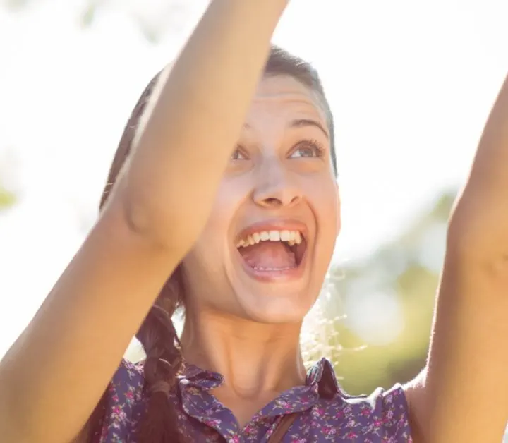 teen girl outside with arms raised up in the air