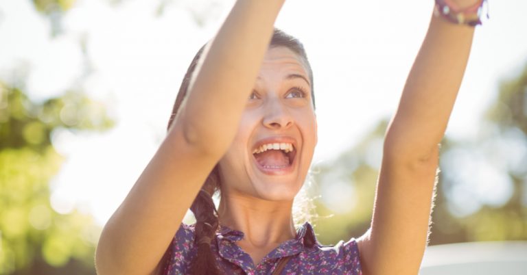 teen girl outside with arms raised up in the air