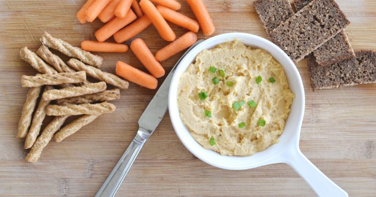 overhead view of Irish pub cheese with green onions sprinkled on top in white bowl with carrots, pretzel sticks and dark bread off to the side