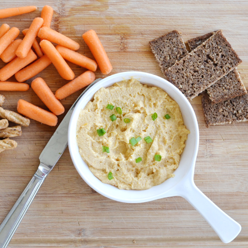 overhead view of Irish pub cheese in white dish with green onions sprinkled on top and carrots, pretzel sticks and dark bread off to the side