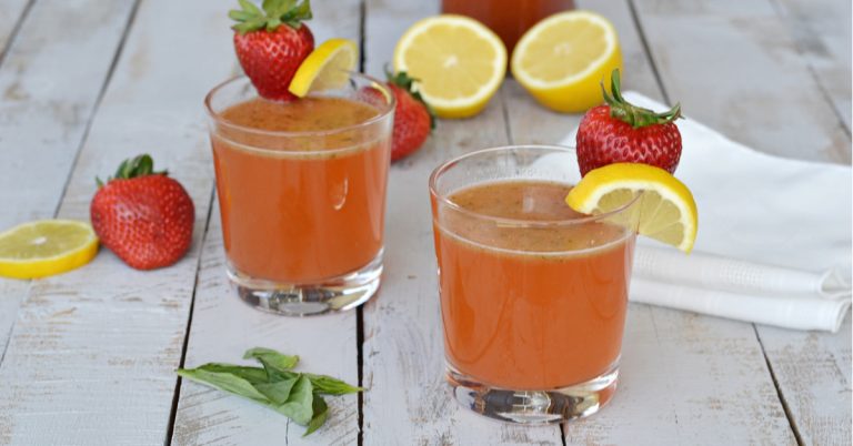 two clear glasses with strawberry lemonade mimosa with lemon on side of glass with basil leaf