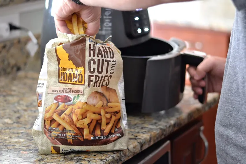 hand getting frozen french fries out of the bag to put in an air fryer