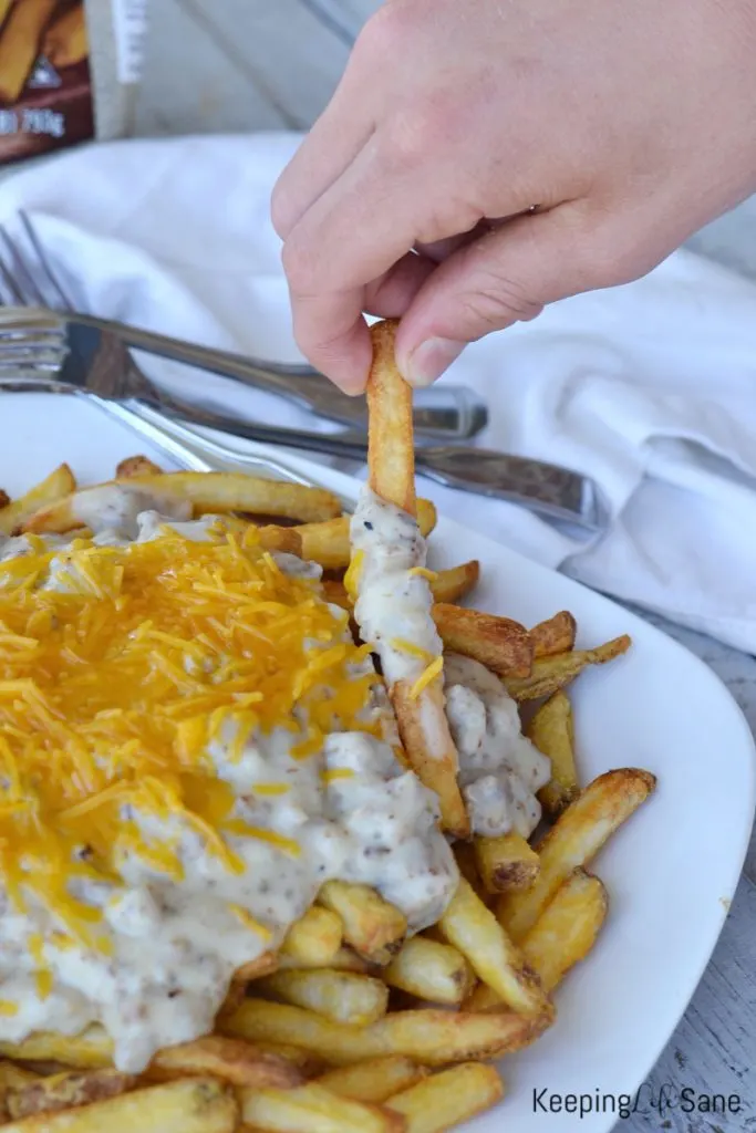 hand grabbing a french fry off a white plate of southern poutine