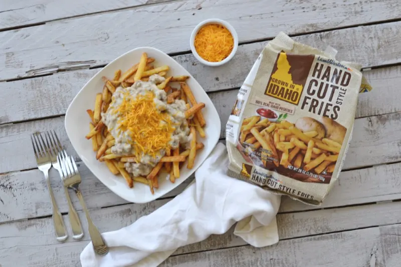overhead view of southern poutine fries on a square plate with a small white bowl of orange shredded cheddar cheese and a bag of hand cut fries