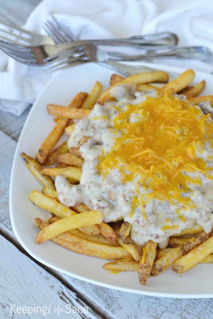 southern poutine fries on a white plate on a grey wooden table, french fries, suasage gravy and shredded chedder cheese