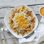 overhead view of southern poutine on white plate on grey wooden table, french fries, suasage gravy and shredded chedder cheese