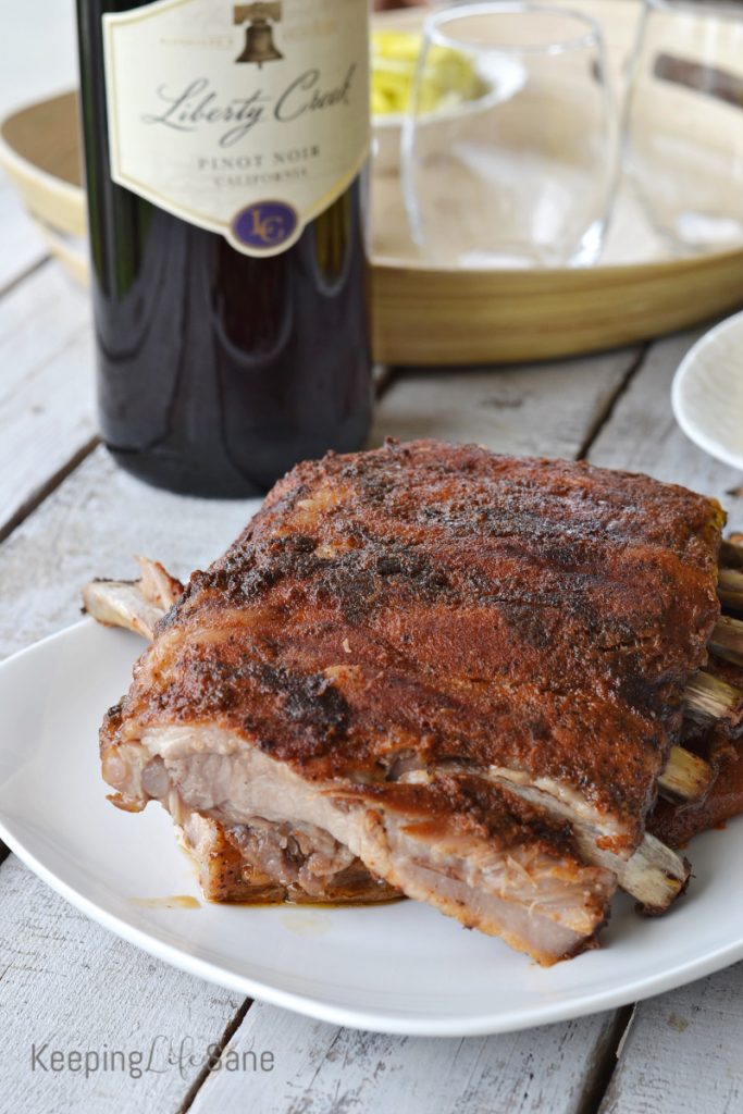 rack of cooked ribs broken in two pieces on white platter with wine bottle in background