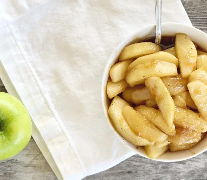 bowl of fried apples from overhead view on a white napkin with a green apple