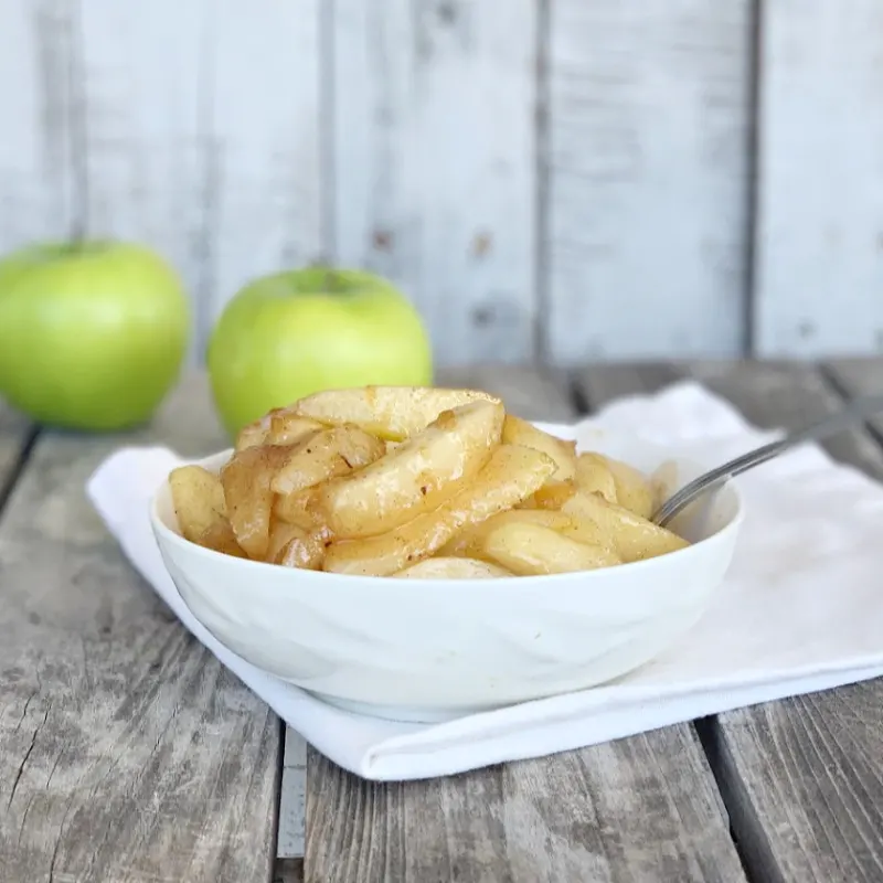 bowl of easy fried apples on a white napkin with a green apple