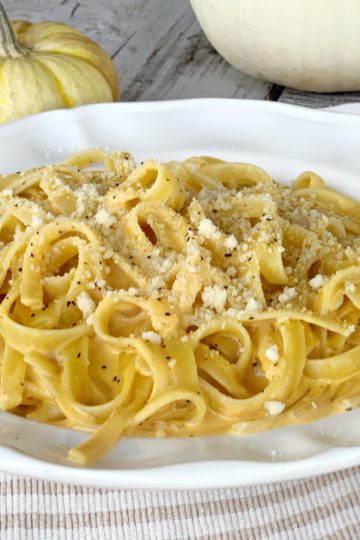 pumpkin alfredo in large round white bowl with parmesan cheese and black pepper on a wooden table