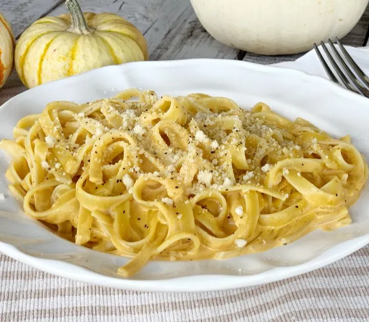 pumpkin alfredo in large round white bowl with parmesan cheese and black pepper on a wooden table