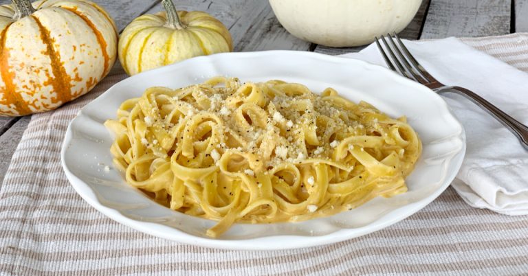 pumpkin alfredo in large round white bowl with parmesan cheese and black pepper on a wooden table