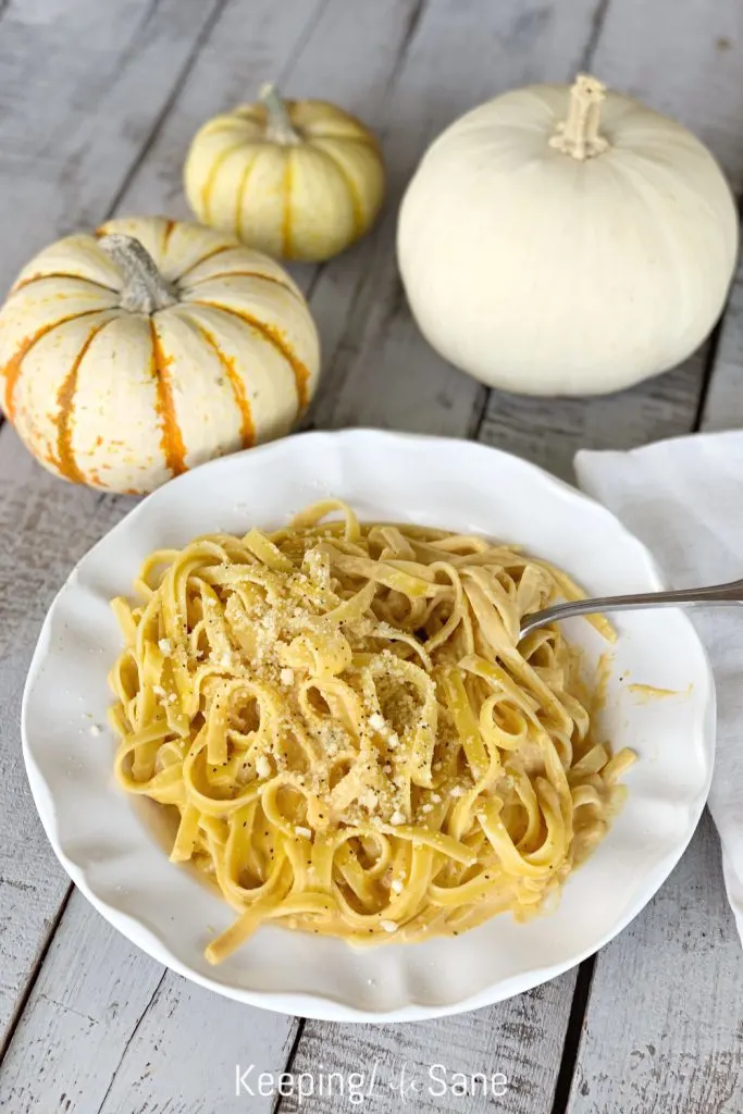 overhead view of pumpkin alfredo in large round white bowl with parmesan cheese and black pepper on a wooden table
