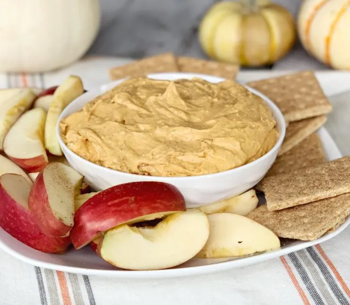 pumpkin pie dip with cream cheese in white bowl on fall tablecloth with apple slice and graham crackers