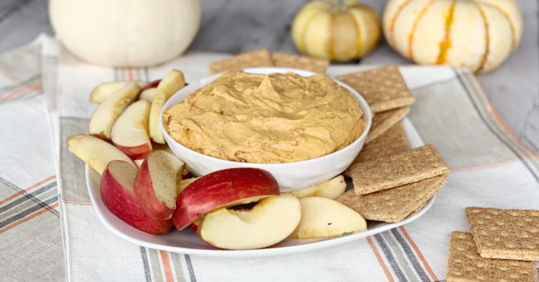 pumpkin pie dip with cream cheese in white bowl on fall tablecloth with apple slice and graham crackers
